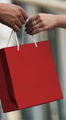 Man hands a red shopping bag to a woman