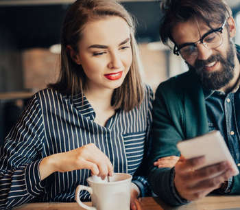 A man and woman look at a phone in a coffee shop