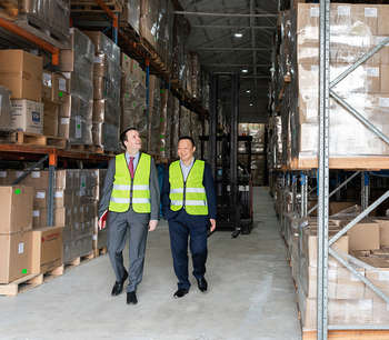 BDO Partner, Ryan Pollett, walks down a warehouse corridor with a client, both wear high-vis jackets