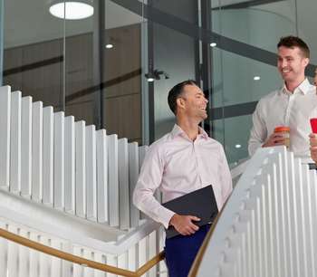 Three BDO employees chat and laugh as they walk down some stairs in an office building