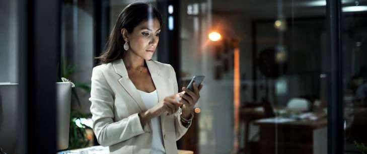 A woman in business attire stands and works on an ipad