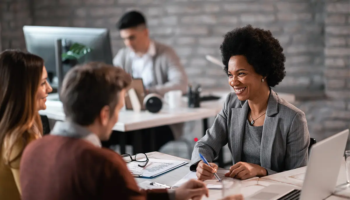 Four people in a room, three people in a meeting being led by a business person.