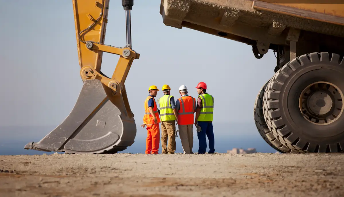Four men standing onsite at a mining project, under a large piece of machinery. 