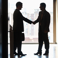 Two business people shake hands, silhouetted by bright light behind them