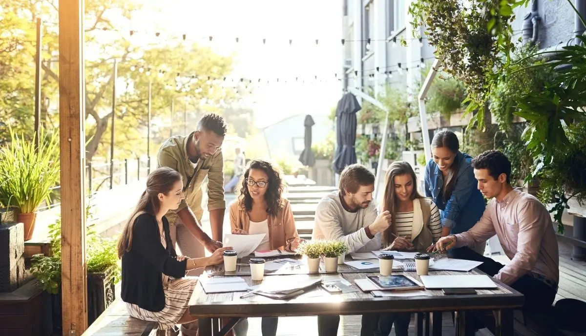 People sitting at a table outside and working on pads of paper and tablets