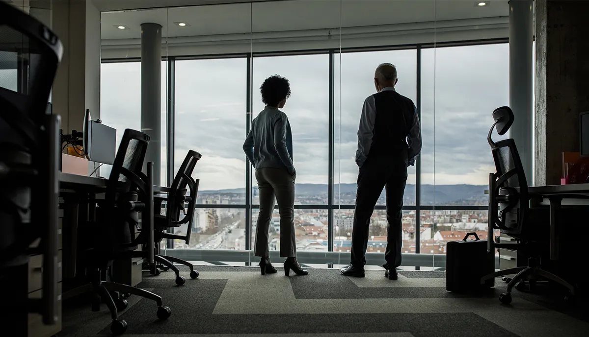Male and female coworkers looking out a window together in the office.