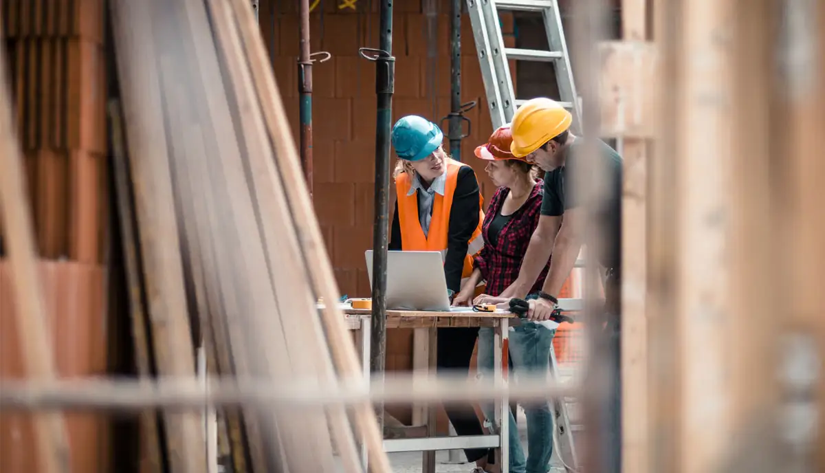 3 people on a construction site, wearing hard hats and high-vis, looking at plans
