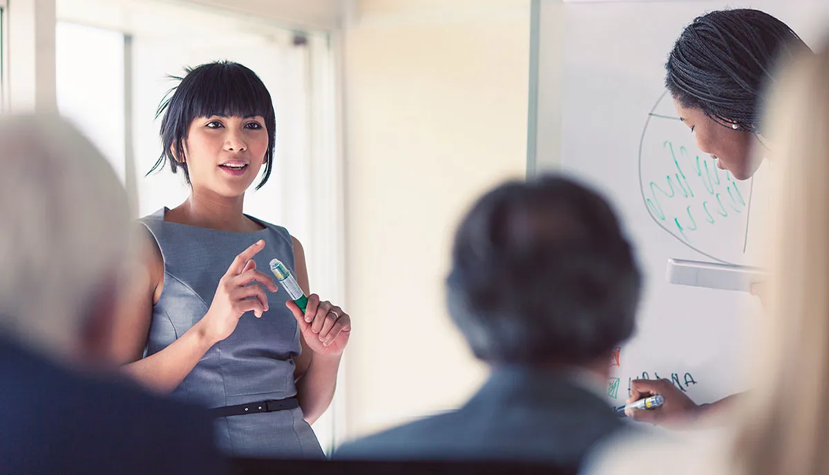 Woman presenting to audience on a whiteboard. 