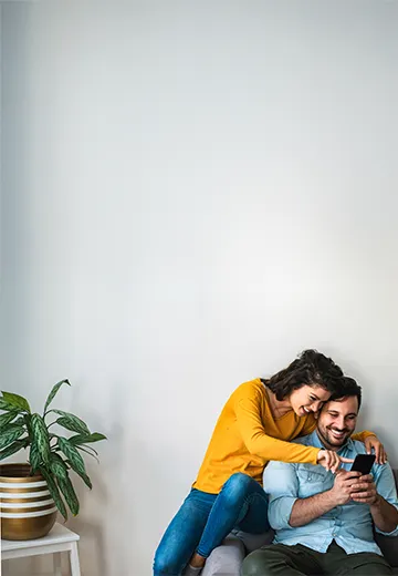 A young couple on a couch looking at their phone.